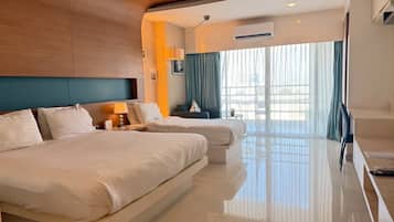 A hotel room with two beds, a sofa, a TV, and a large window with curtains.