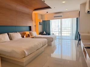 Habitación de hotel con dos camas, un sofá, un televisor y un ventanal grande con cortinas.