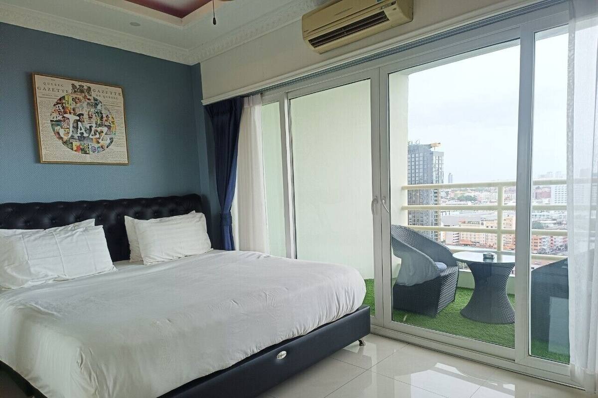 Une chambre avec un grand lit, une vue sur la ville grâce à une porte-fenêtre coulissante et un ventilateur de plafond.
