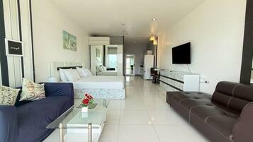 Ein modernes Hotelzimmer mit Bett, Sofa, Couchtisch, Fernseher und Blick auf die Stadt.