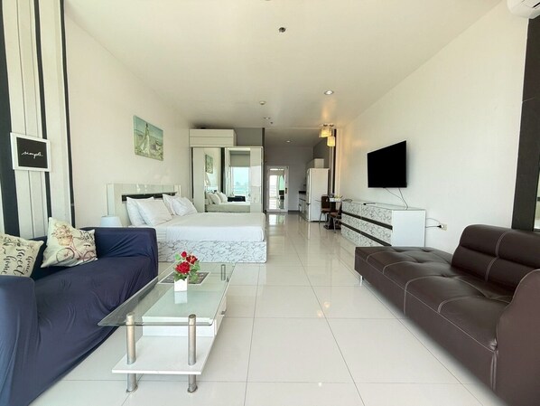 A modern hotel room with a bed, sofa, coffee table, TV, and a view of the city. - View Talay 6 Condominium by Honey (Pattaya)