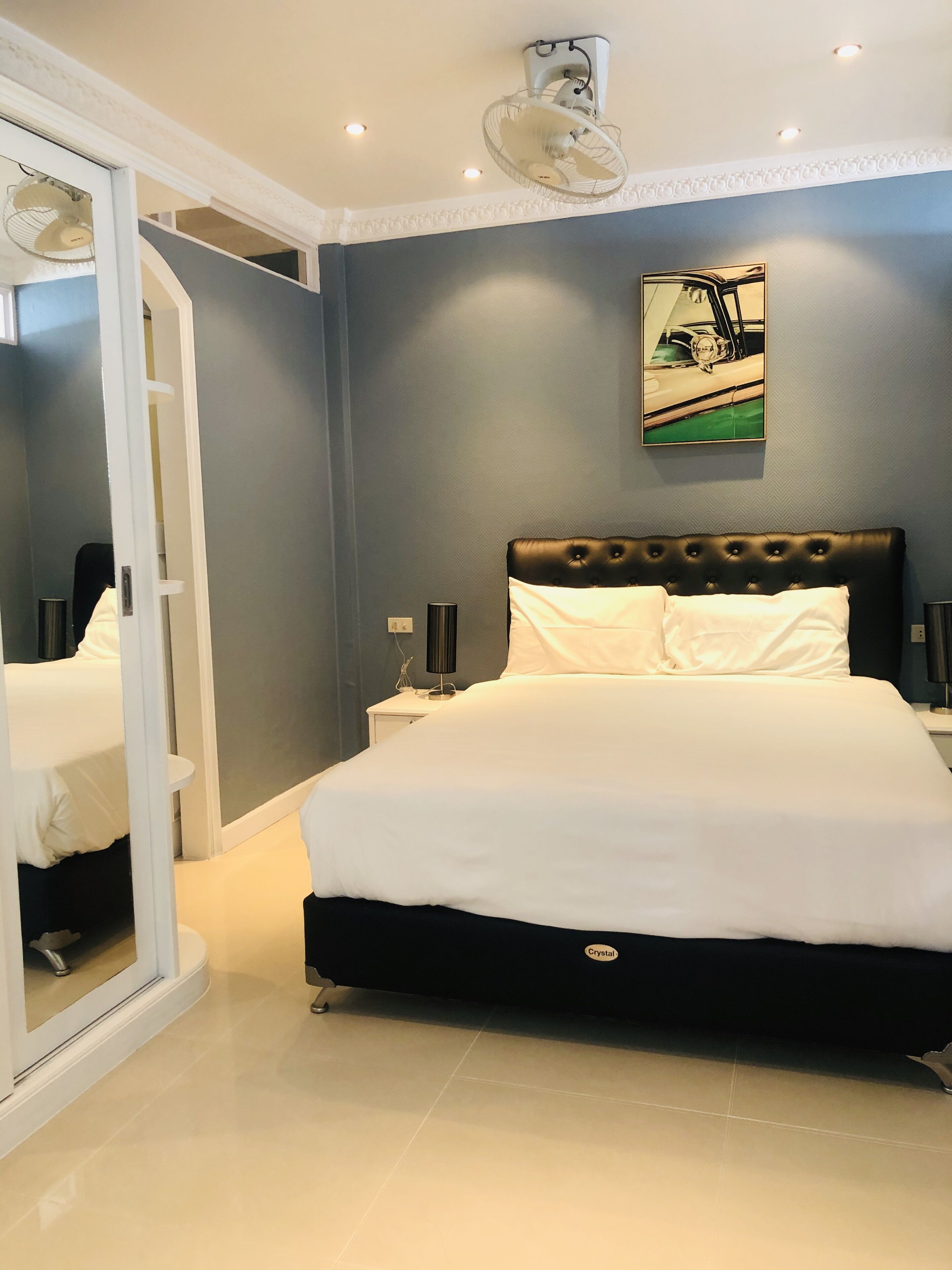 A bedroom with a large bed, a ceiling fan, recessed lighting, a painting on the wall, and a sliding door leading to another room.