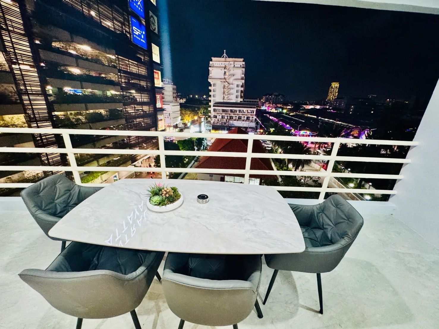 A balcony with a table and chairs, overlooking a cityscape at night.