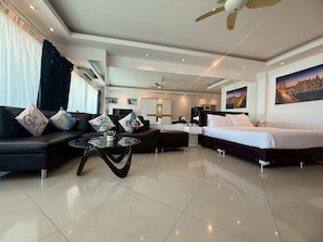 A modern hotel room with a sofa, a coffee table, a bed, and a cityscape painting. - View Talay 6 Condominium by Honey (Pattaya)