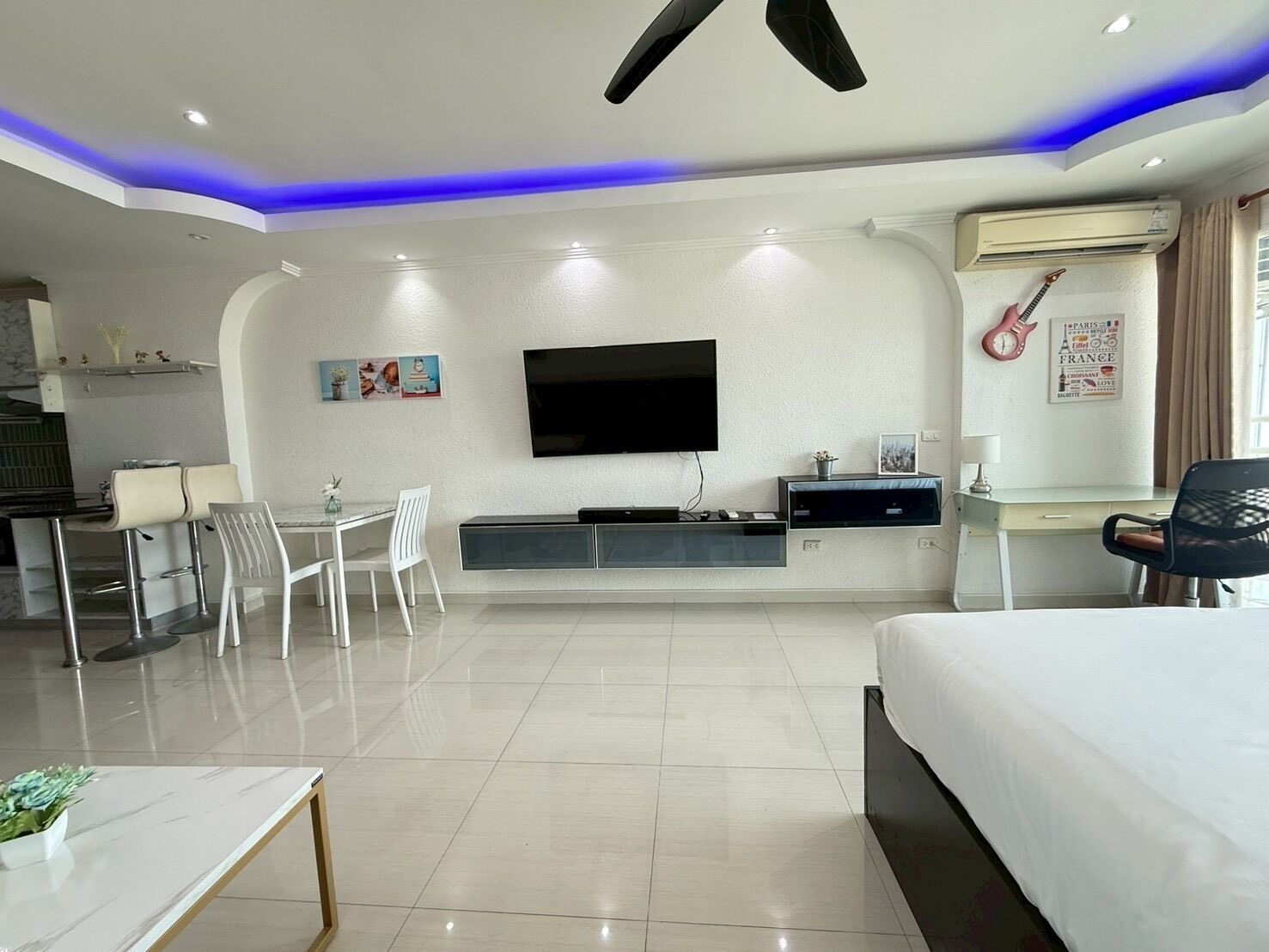 Una habitación de hotel moderna con televisión de pantalla plana, una cama, un escritorio con silla, y un área de comedor con sillas.