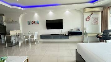 Una habitación de hotel moderna con televisión de pantalla plana, una cama, un escritorio con silla, y un área de comedor con sillas.