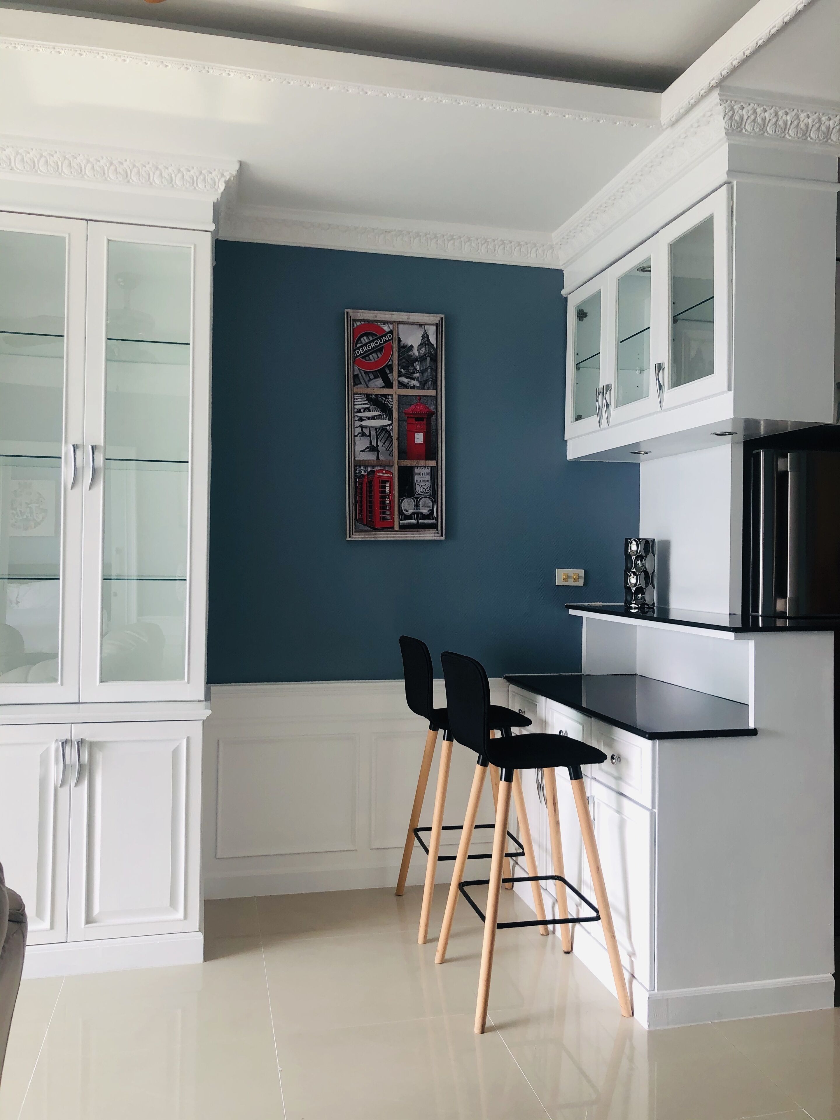 A modern kitchen with white cabinetry, a blue accent wall, and a framed picture of London landmarks.
