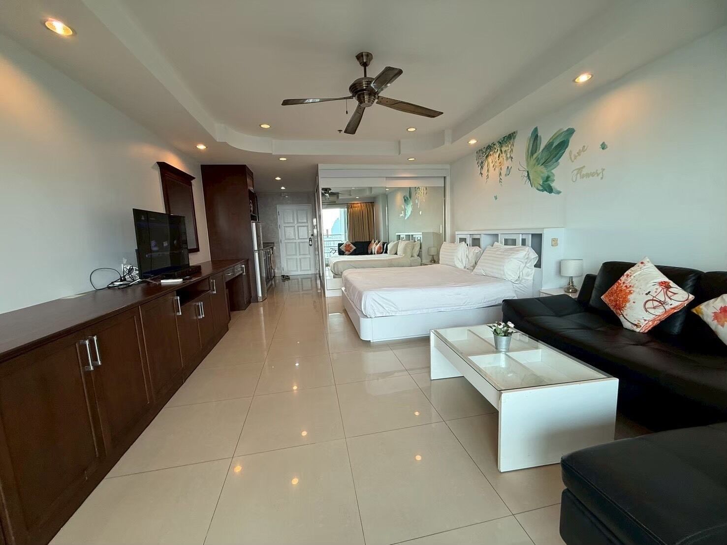 A hotel room with a bed, a sofa, a coffee table, a TV, and a ceiling fan.