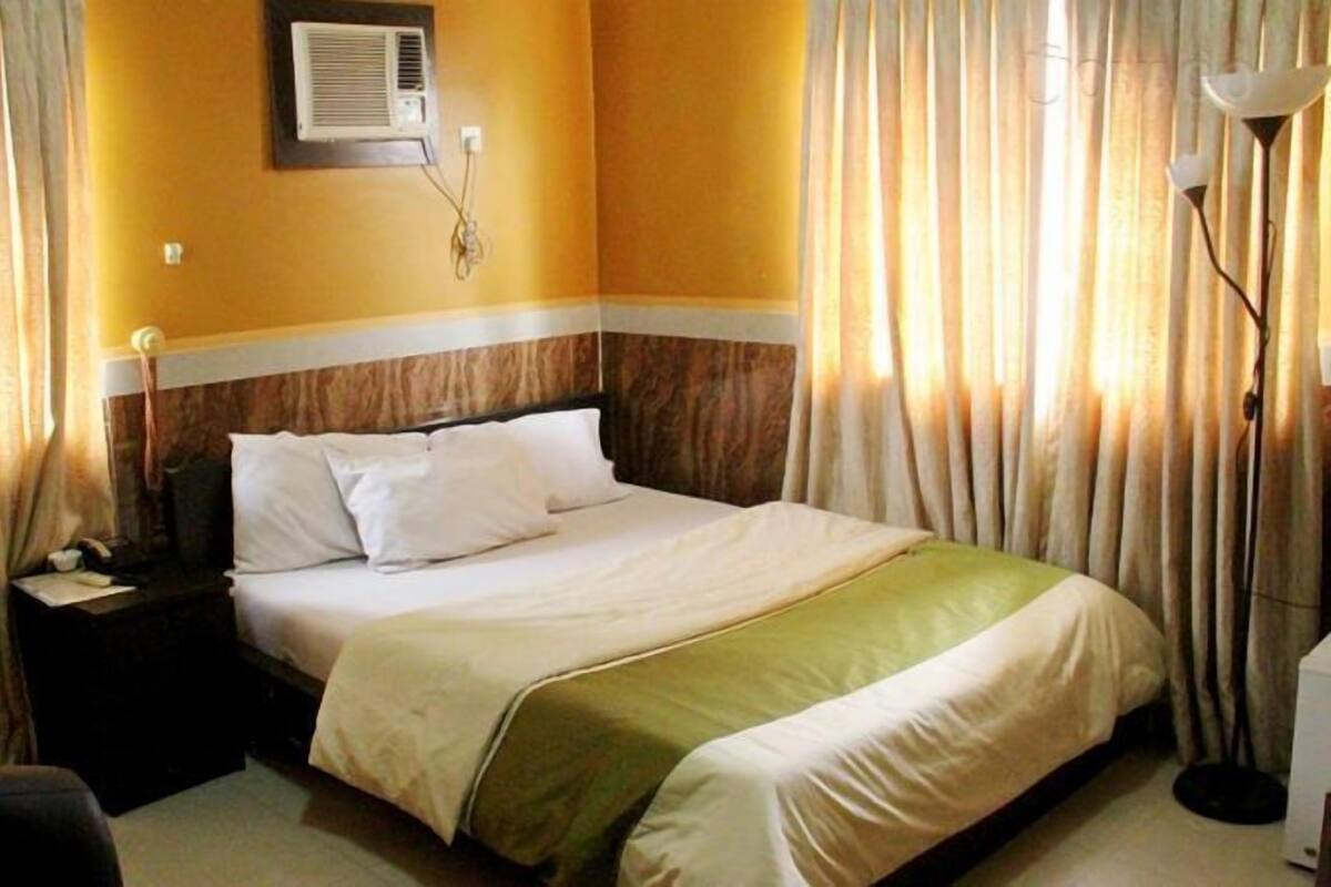 A hotel room with a bed, a nightstand, a lamp, and curtains.
