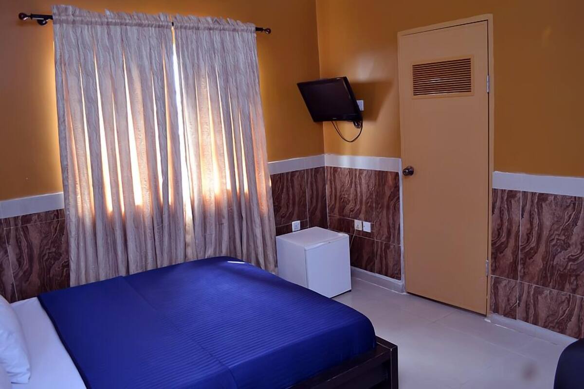 A hotel room with a bed, a TV mounted on the wall, a door, and a small white cabinet.
