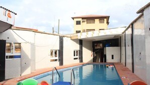 Una piscina con plataforma de baldosas, una ventana pequeña y un edificio al fondo.