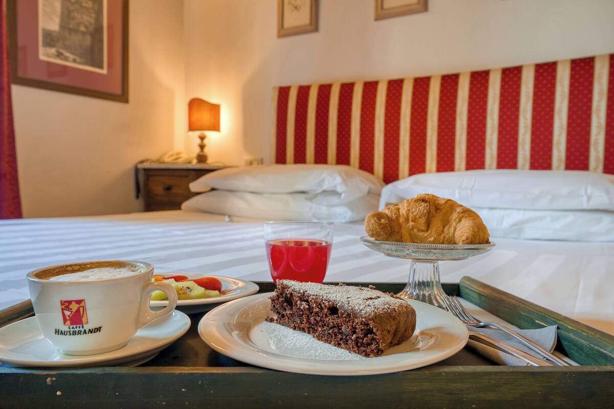 A breakfast setup with a croissant, a slice of cake, a cup of coffee, and a glass of red beverage on a tray.