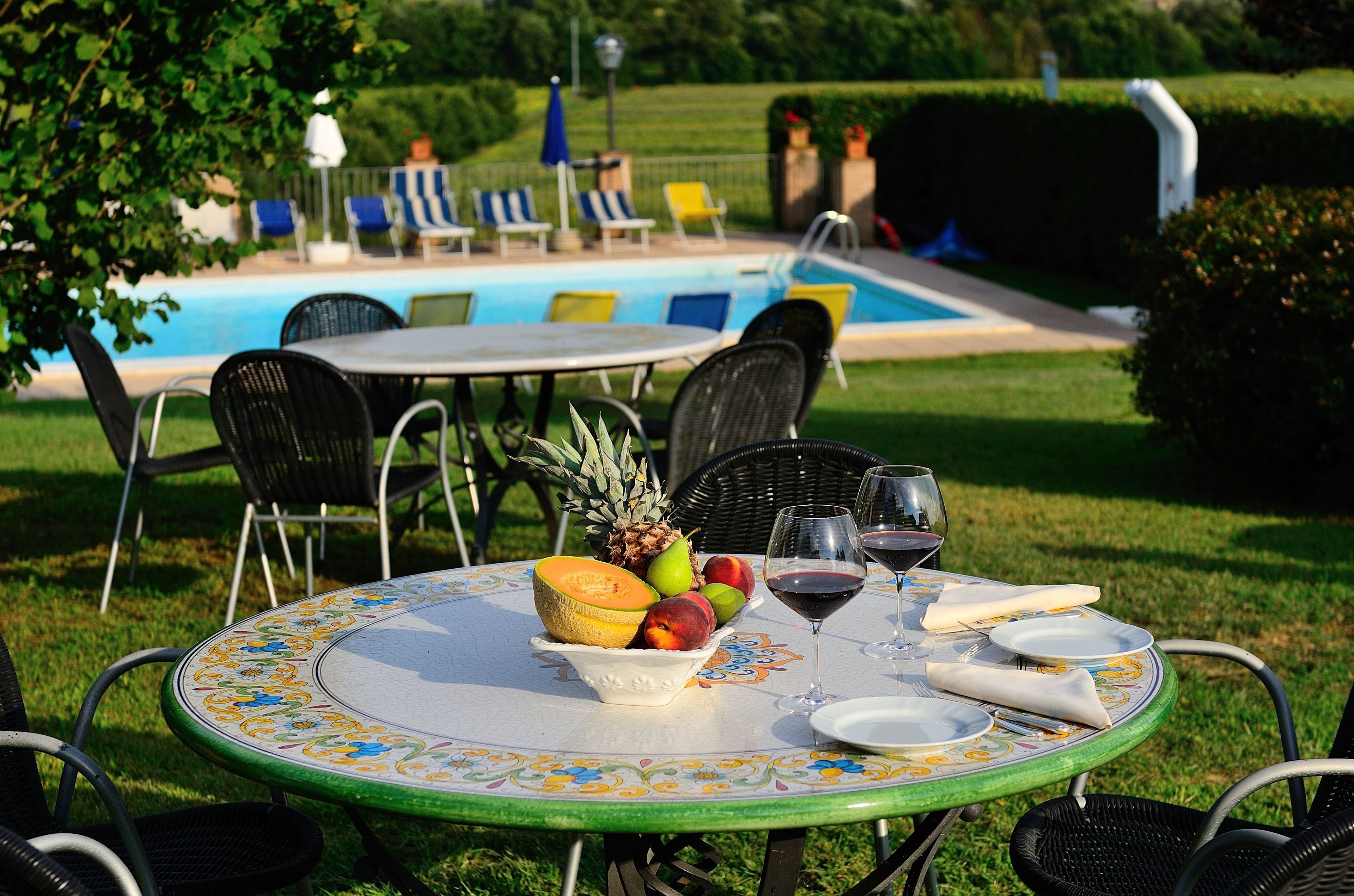 An outdoor dining area with a table set for two, surrounded by chairs, near a swimming pool.