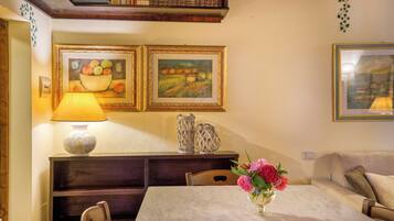 A dining area with a table, chairs, a lamp, and two framed paintings on the wall.
