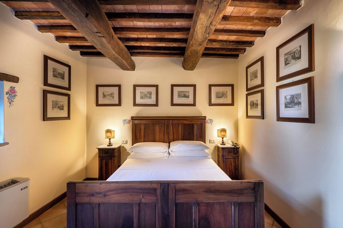 A bedroom with a wooden bed, framed pictures on the walls, and wooden beams on the ceiling.