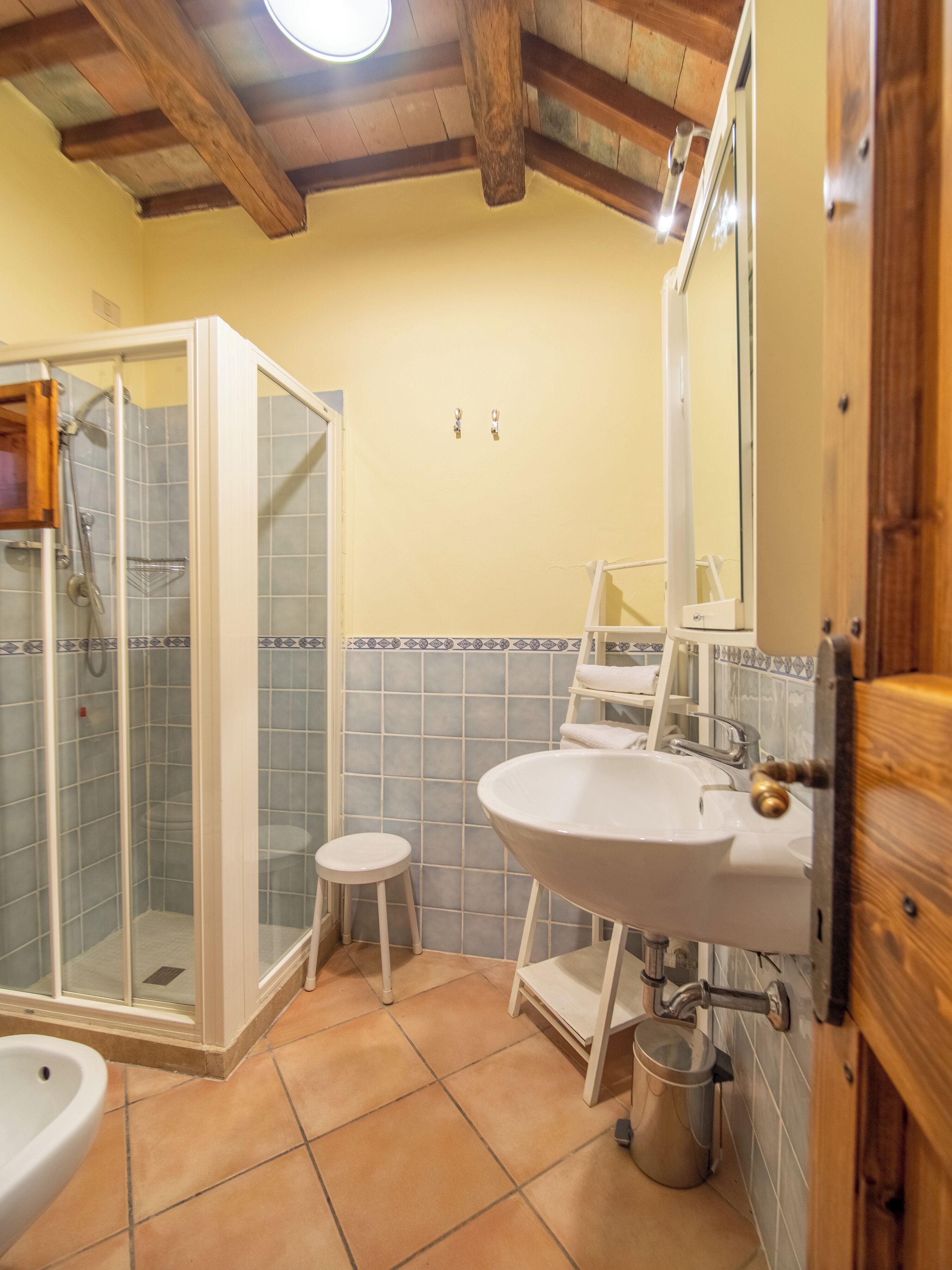 Un baño con ducha, inodoro, lavabo y un taburete pequeño.