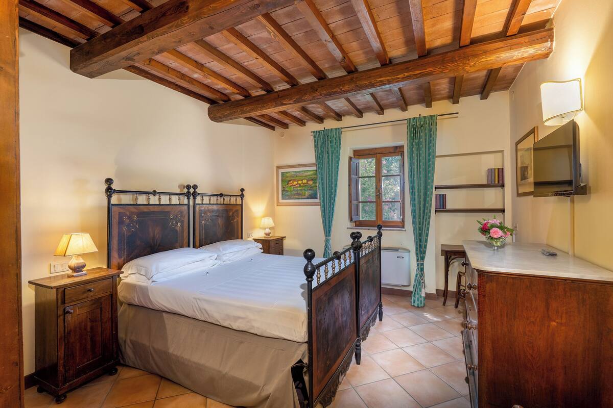 A bedroom with a wooden bed, bedside tables, a dresser, a mirror, and a window with curtains.