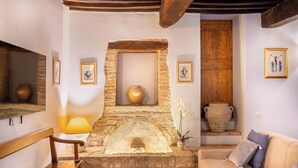 A cozy room with a stone fireplace, wooden beams, a cushioned bench, and a sofa. - Borgo Mandoleto (Perugia)