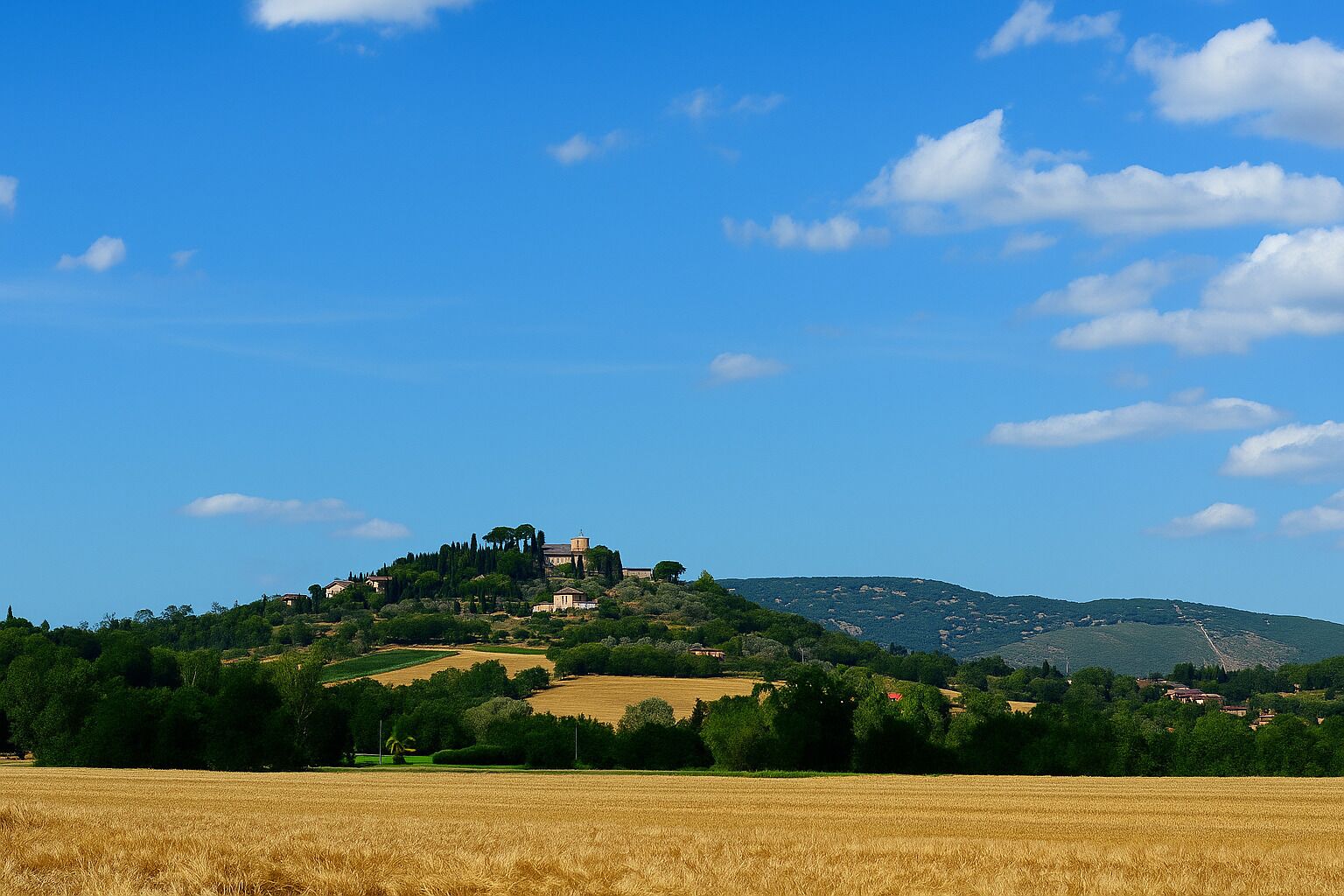Un paisaje rural con una edificación en la cima de una colina, rodeado de campos y árboles.