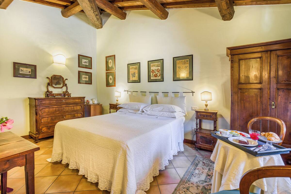 A bedroom with a bed, dresser, bedside tables, and a breakfast table with food and drinks.