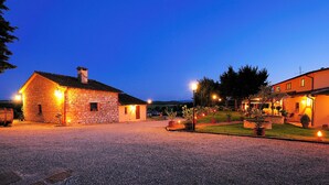 A stone building with a gravel driveway, a well-lit garden, and a clear evening sky. - Borgo Mandoleto (Perugia)