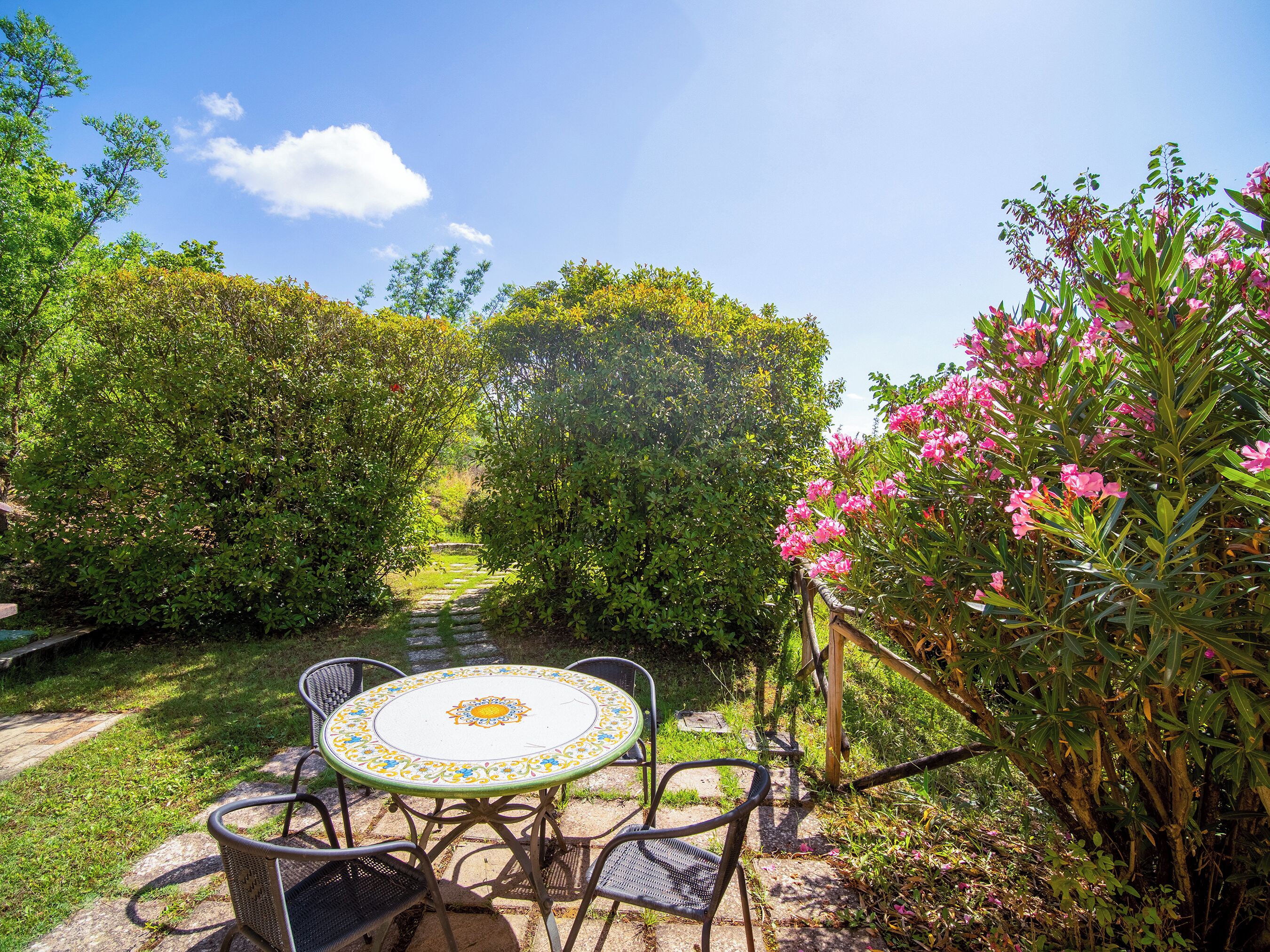 A garden patio with a round table and four chairs, surrounded by lush greenery and flowering plants.