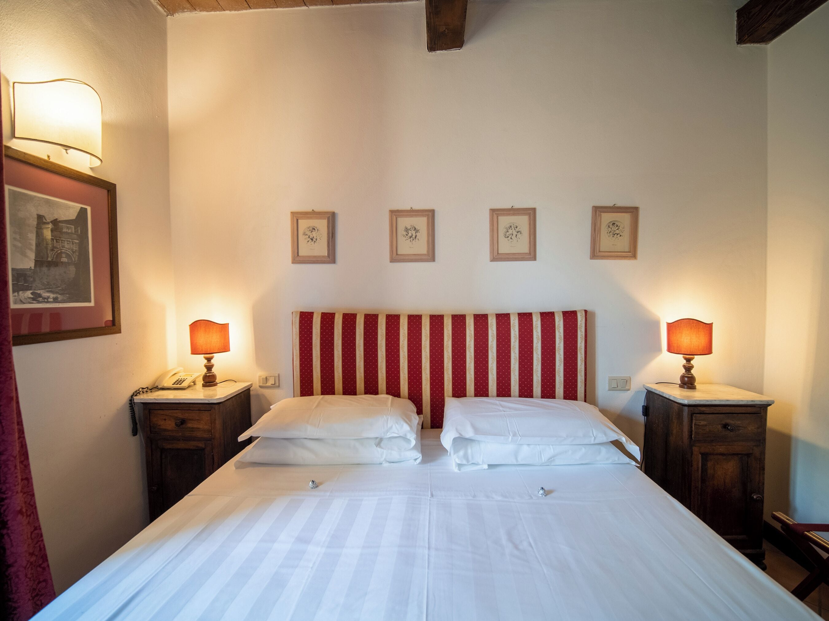 Une chambre d’hôtel avec un lit double, deux tables de chevet avec des lampes, une tête de lit à motifs rayés et quatre tableaux encadrés accrochés au mur.