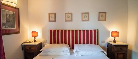 Une chambre d’hôtel avec un lit double, deux tables de chevet avec des lampes, une tête de lit à motifs rayés et quatre tableaux encadrés accrochés au mur.