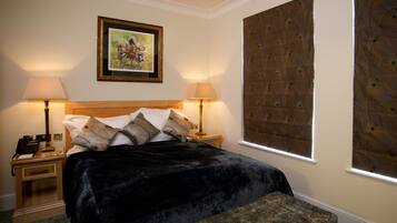 A hotel room with a large bed, two bedside lamps, a nightstand with a telephone, a framed painting on the wall, and a window with a decorative blind.