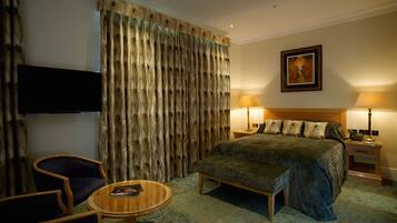 A hotel room with a bed, a desk, a chair, a TV, and two lamps.