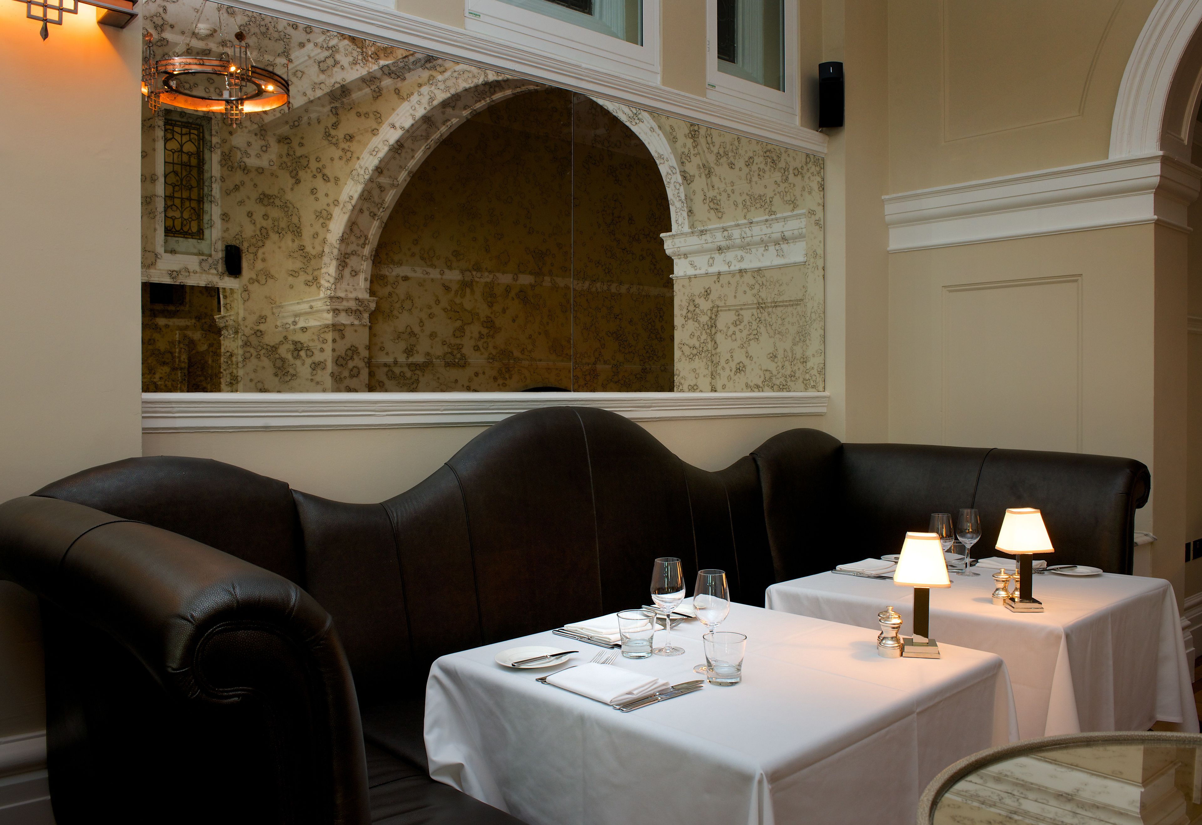 A dining area with leather booths, white tablecloths, and candlelit lamps.