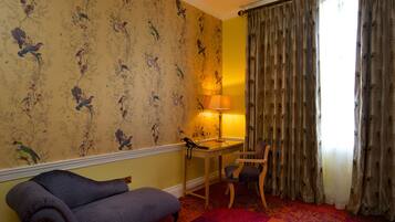 A room with a floral wallpaper, a desk with a lamp, a chair, and a sofa.