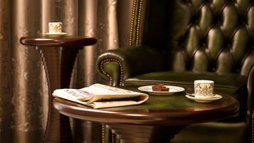 A room with a green leather armchair, a small round table with a book and a teacup, and a side table with a teacup and a book.