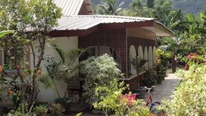 Une maison avec un toit en pente, entourée d’une végétation luxuriante et d’un jardin.