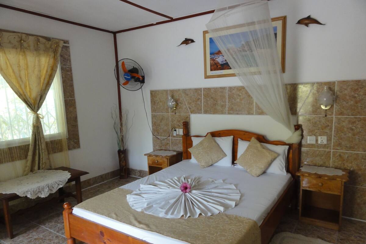 A neatly arranged bedroom with a bed, bedside tables, a wall-mounted fan, and a decorative wall hanging.