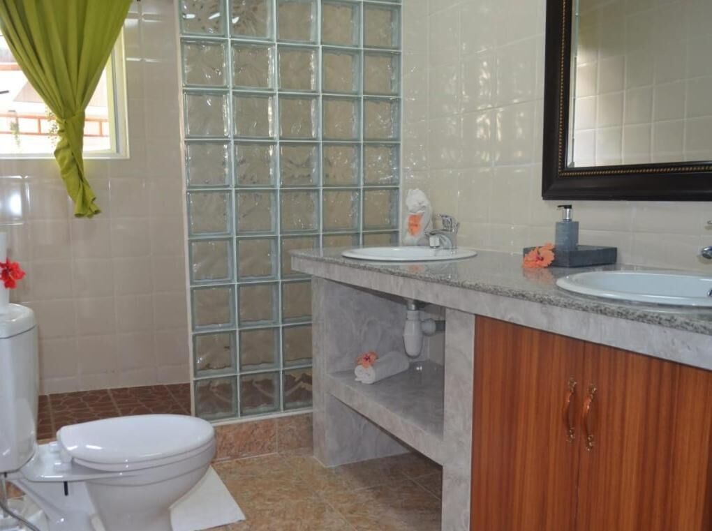 Ein Badezimmer mit Toilette, Waschbecken, Spiegel und Duschbereich mit Glastür.