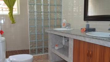 Ein Badezimmer mit Toilette, Waschbecken, Spiegel und Duschbereich mit Glastür.