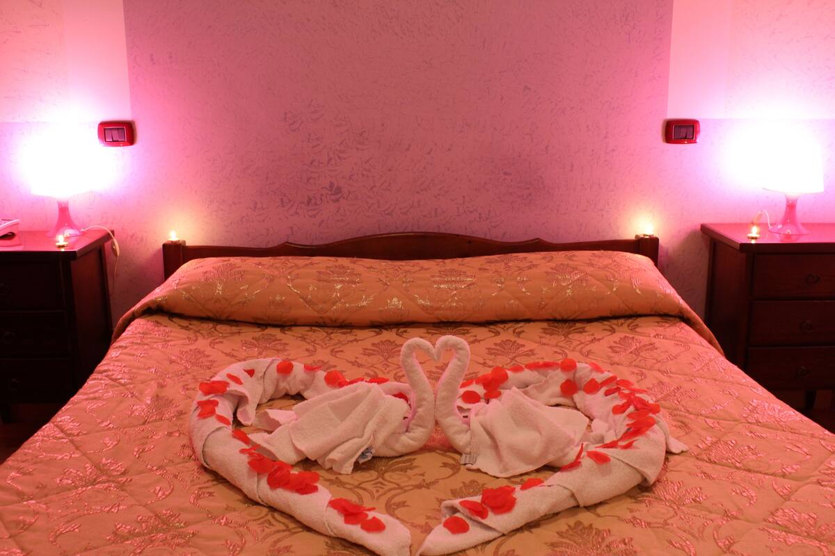 A bed with a heart-shaped towel arrangement and two bedside lamps.