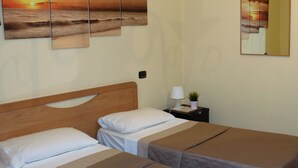 Een hotelkamer met twee bedden, een nachtkastje met een lamp en een plant, en een groot schilderij van een zonsondergang aan de muur.
