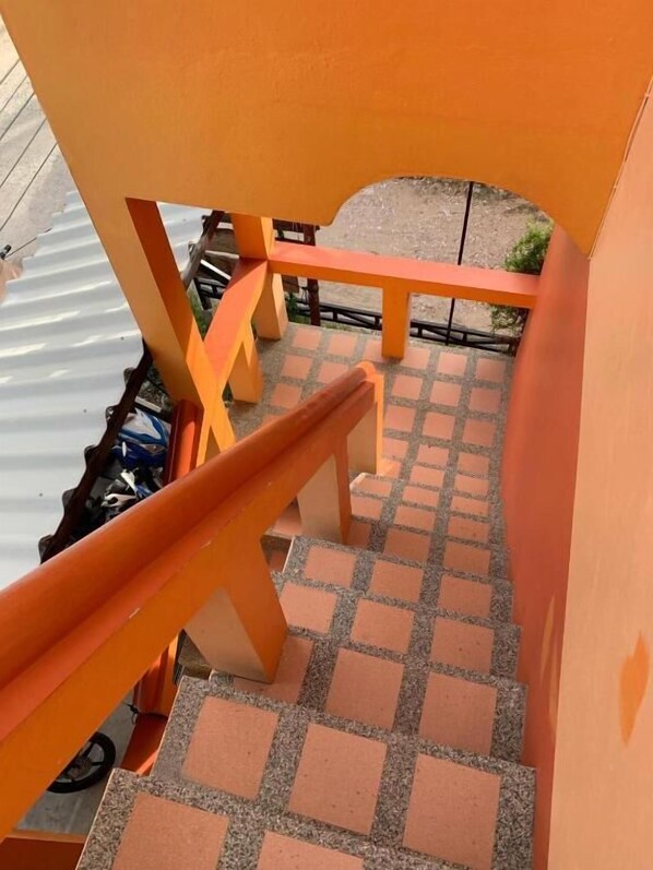 A staircase with orange railings leading to a covered outdoor area with a tiled floor.