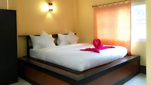 A hotel room with a large bed, a wall-mounted air conditioner, a nightstand, and a window with curtains. - Sarin Guesthouse (Koh Tao)