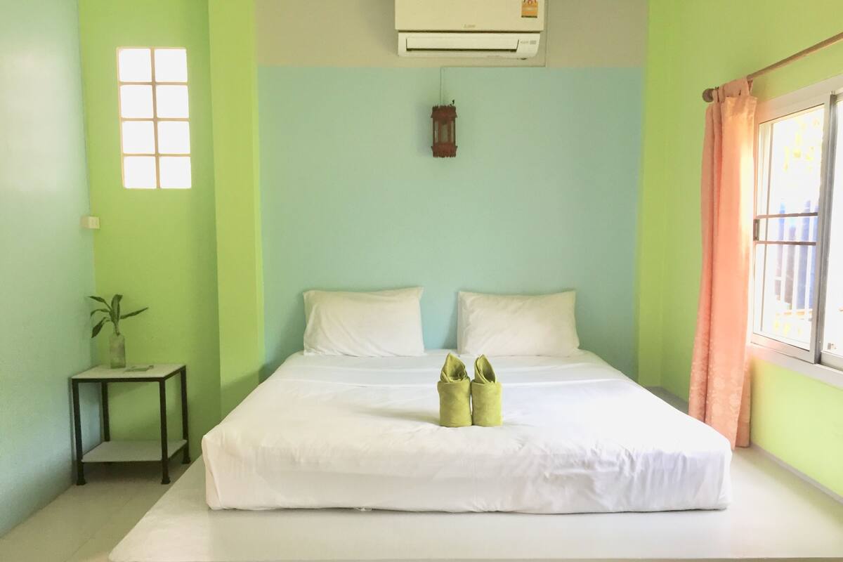 A room with a bed, a small table with a plant, and a window with curtains.