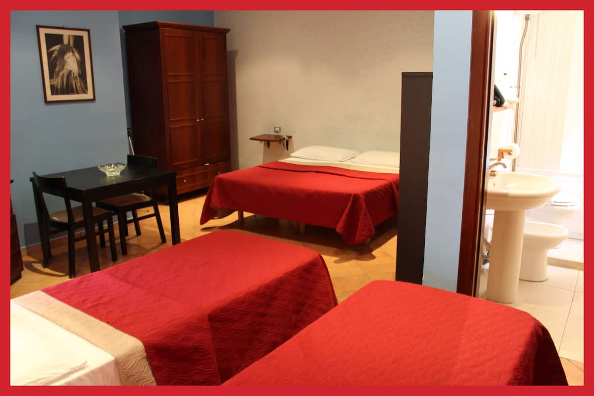 A room with two beds, a wooden cabinet, a desk with a chair, and a bathroom with a sink and toilet.