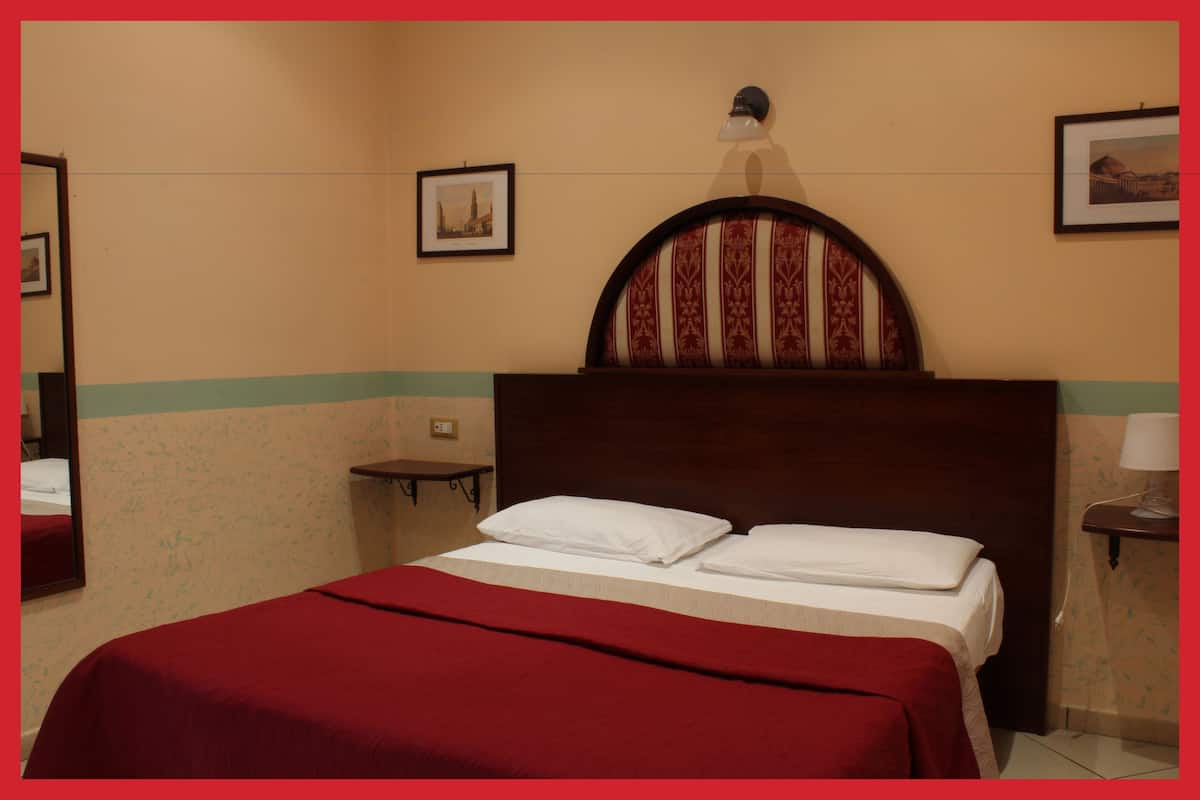 A hotel room with a bed, a nightstand, and a wall-mounted lamp.