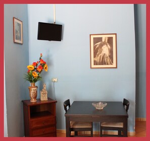 Een eetgedeelte met een tafel, stoelen, een vaas met bloemen, een klein kasteelmodel en twee ingekaderde foto's aan de muur.