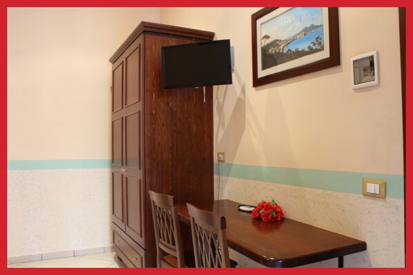 A small dining area with a wooden table, two chairs, a bouquet of red flowers, a television mounted on the wall, and a framed picture above the table. - B&B La Storia di Napoli (Naples)