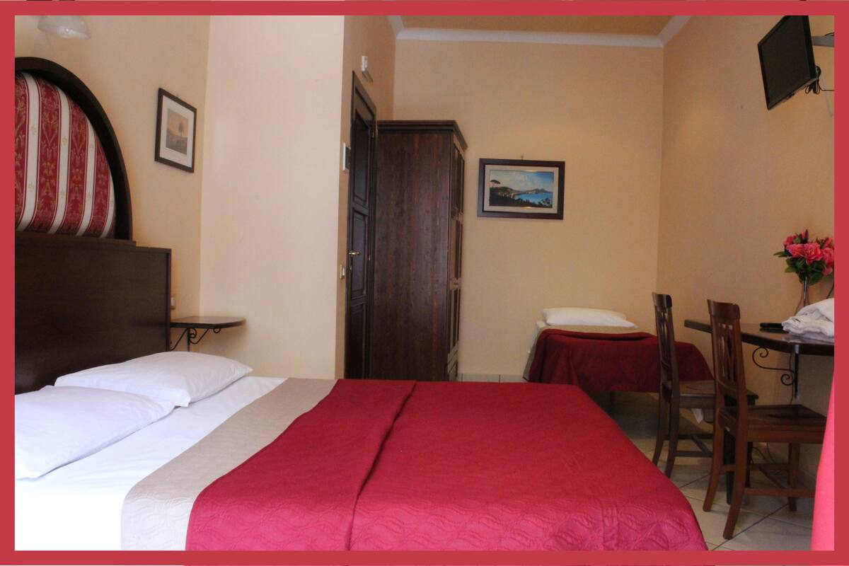 A hotel room with a bed, a desk, a chair, a wardrobe, and a picture on the wall.