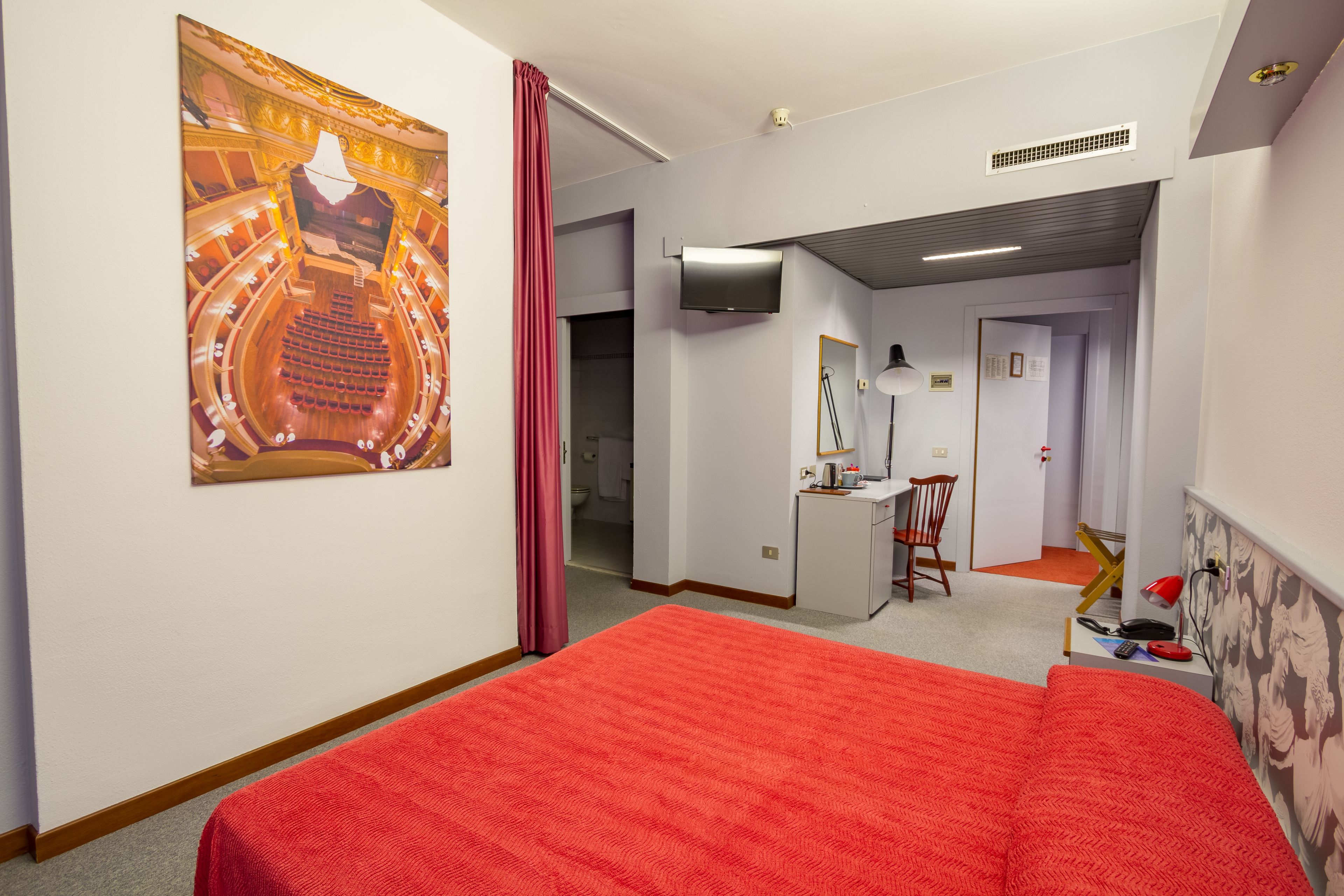 A hotel room with a large bed, a desk, a chair, a TV, and a bathroom visible through an open door.