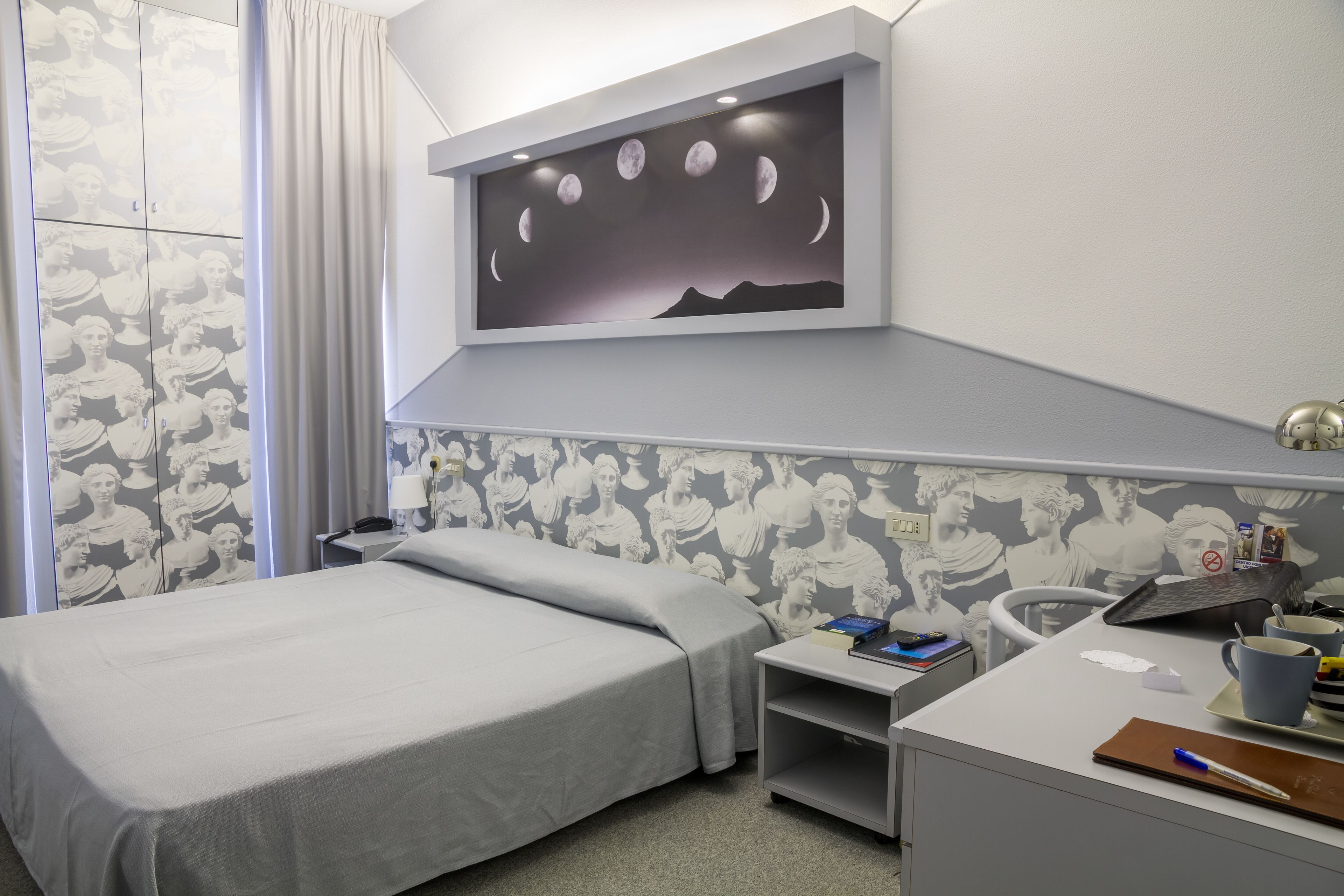 Une chambre d’hôtel comprenant un lit, un bureau avec une chaise, une table de chevet et un téléviseur fixé au mur qui affiche les phases de la lune.