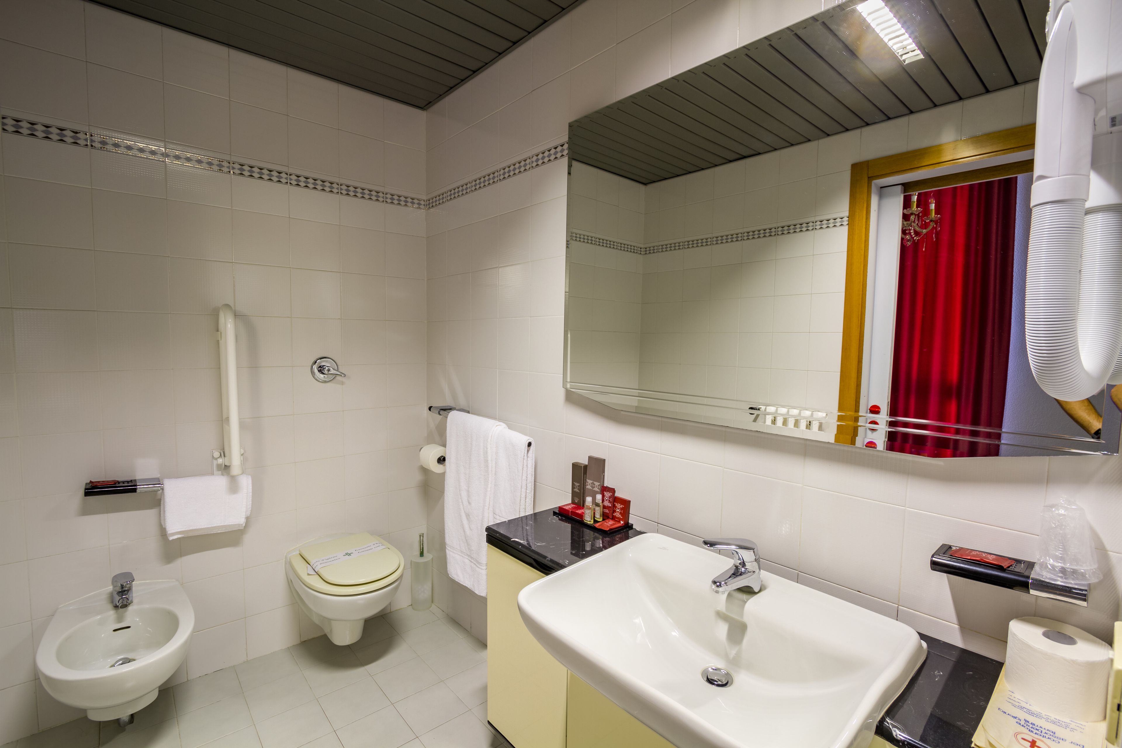 Un bany amb vàter, bidet, rentapel i un mirall amb cortina vermella.